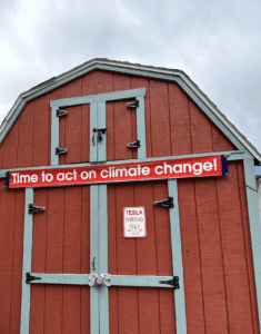 A banner reading"Time to act on climate change!" hangs above the doors to red tool shed designed to look like a barn. 